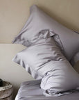 Gray satin pillowcases on a bed against a beige wall - TENCEL™ Lyocell