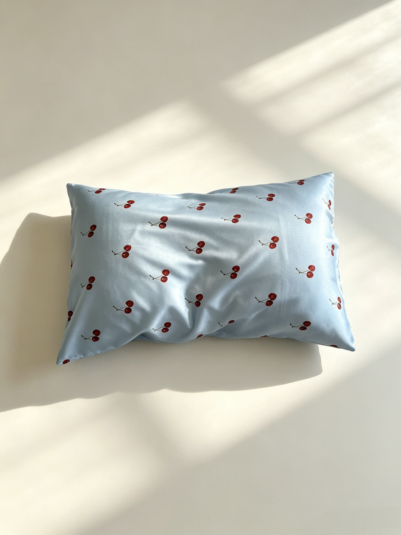 Light blue silk pillowcase with red cherry pattern on a white surface