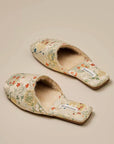 Pair of beige floral slippers with fluffy cream-colored lining. The slippers have a square toe and feature a delicate floral pattern in shades of orange, green, and white. The brand name &