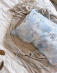 A soft sky blue silk pillowcase on a bed, featuring an artistic design of round Chinese hand-fan motifs and ink-painted landscape patterns. silk pillow cases