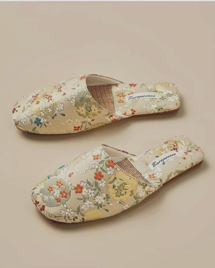Pair of beige floral women slippers have a squared toe and are made of a floral patterned fabric.  The insole is visible and appears to be made of woven material. A small tag with the word &#39;Europeeve&#39; is visible on each slipper.