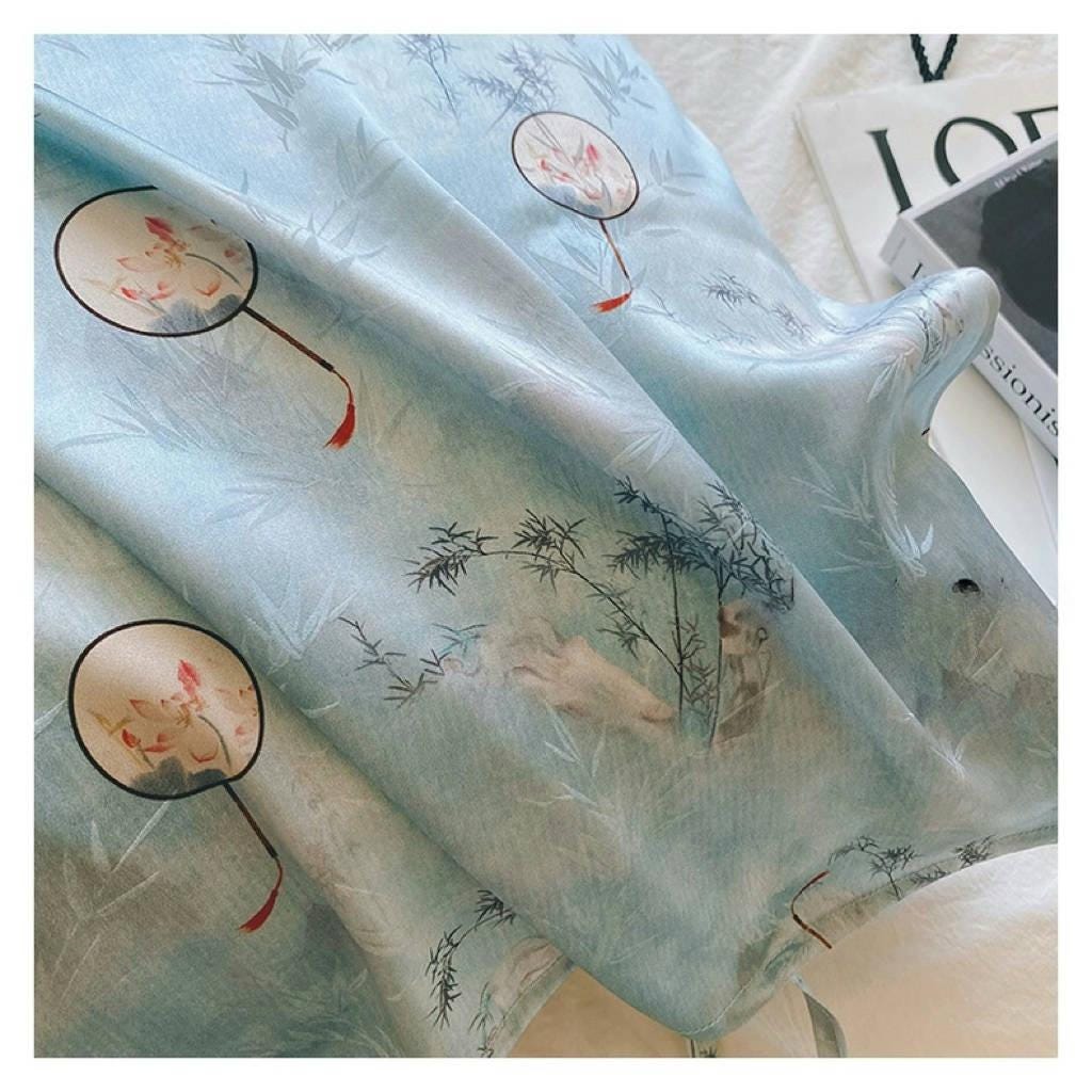 A soft sky blue silk pillowcase on a bed, featuring an artistic design of round Chinese hand-fan motifs and ink-painted landscape patterns.