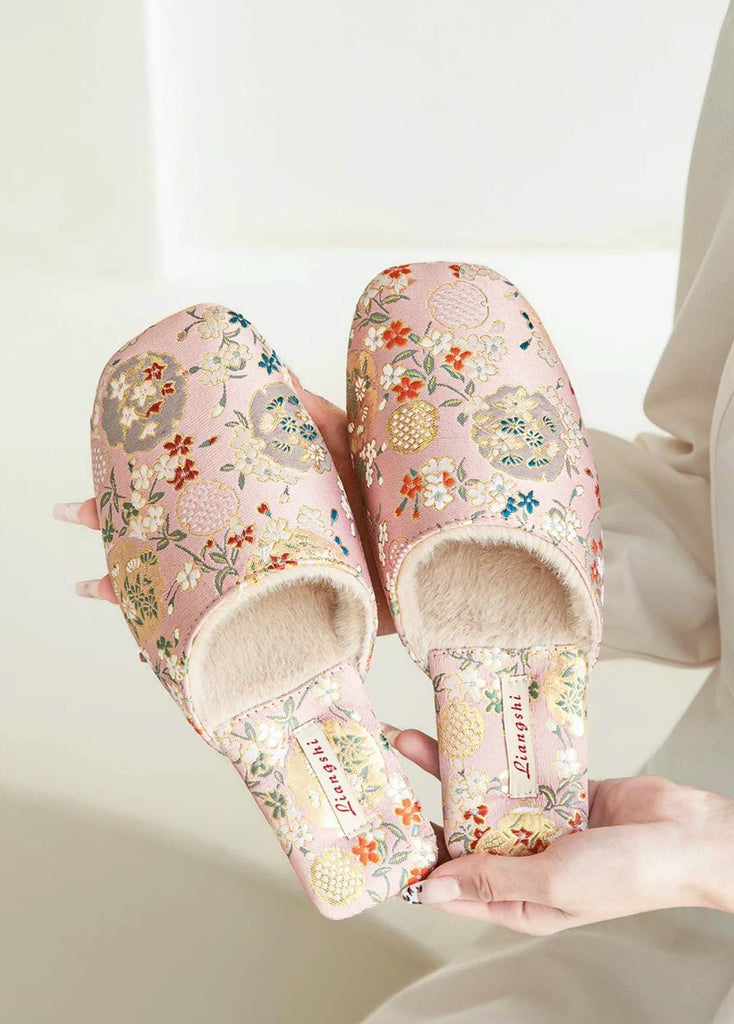 Pink floral slippers with a plush, light beige interior. The slippers feature an embroidered floral pattern in shades of pink, orange, and gray. The brand name &#39;Liangshi&#39; is embroidered on the insole. These comfortable and stylish slippers are perfect for relaxing at home.